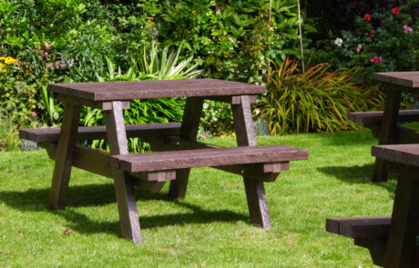 Small brown picnic tables set on grass by a flowerbed