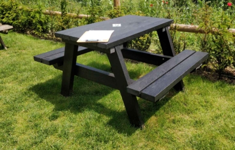 Outdoor restaurant picnic bench in black on grass.